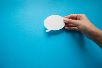 Speech bubbles on blue paper background.  Hand holding a speech balloon.