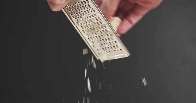 Slow motion closeup of grating aged parmesan over dark background