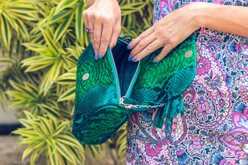 Closeup woman hands with fashion luxury snakeskin python handbag. Outdoors, Bali island.
