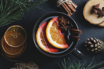 Top view of sweet hot mulled wine in the big black mug on the black table decorated spices, dried...