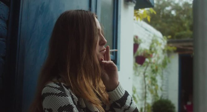 Portrait of young pretty teenage girl smoking cigarette in the backyard in the evening. 4K UHD RAW edited footage