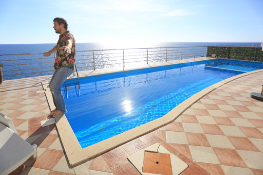 A Man In Jeans And A Shirt Falls Backward Into The Sea View Pool