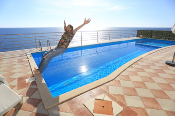 a man in jeans and a shirt falls backward into the sea view pool