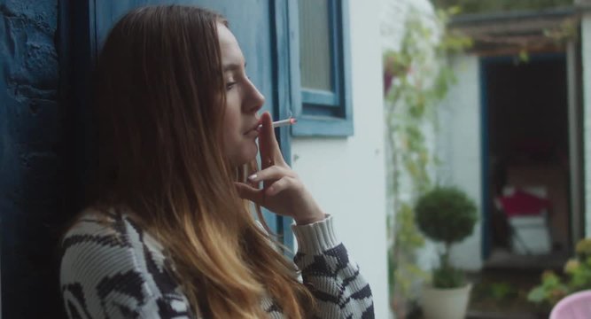 Portrait of young pretty teenage girl smoking cigarette in the backyard in the evening. 4K UHD RAW edited footage