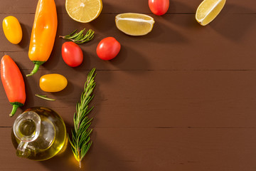Olive oil, tomato, lemon, pepper and herbs on dark wooden table. Top view.