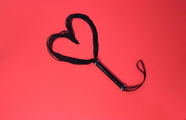 Black whip on a red background is made in the form of a heart. Valentine's Day.