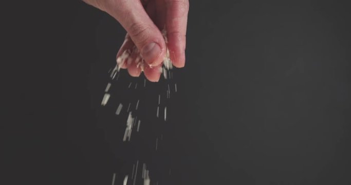 Slow motion closeup of man hand sprinkle grated aged parmesan over dark background