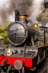 Naklejka premium Steam Engine. Heritage steam engine in steam, waiting under the coal hopper to refill its tender on a busy heritage steam railway.