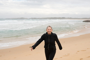 Happy older woman in black clothing laughing at beach on winter's day (selective focus)