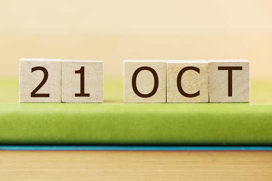 Wooden cube shape calendar for OCT 29 on green book, table.  