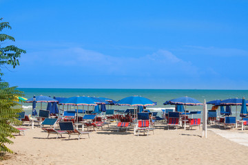 Adriatic Sea coast view. Seashore of Italy, summer umbrellas on sandy beach with clouds on horizon.