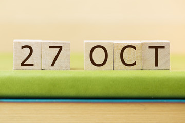 Wooden cube shape calendar for OCT 29 on green book, table.  
