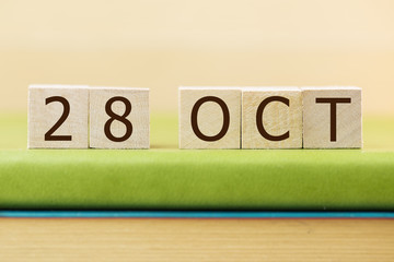 Wooden cube shape calendar for OCT 29 on green book, table.  