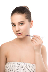 Fototapeta premium Portrait of beautiful young brunette woman with clean face. Beauty spa model girl with perfect fresh clean skin applying cosmetic brush. Youth and skin care concept. Isolated on a white background.
