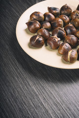 Fried brown chestnuts on a yellow plate on a beautiful dark table.