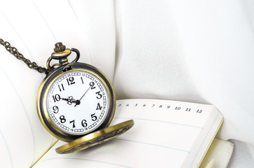 Vintage pocket watch with notebook on white fabric background