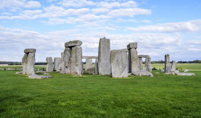 Fototapeta na wymiar Stonehenge prehistoric monument, green grass, blue sky and clouds - Wiltshire, Salisbury, England, UK