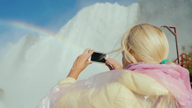 A woman in a raincoat is photographing the Niagara Falls. Tourism in the USA and Canada concept