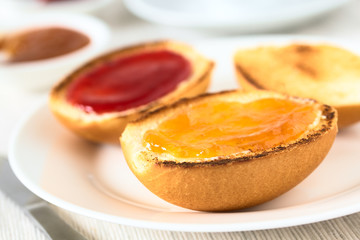 Continental breakfast consisting of toasted bread rolls with butter, peach and strawberry jam, photographed with natural light (Selective Focus on the front of the peach jam on first roll)