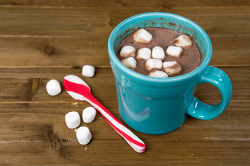hot chocolate drink in turquoise mug on wood with red striped peppermint Christmas spoon