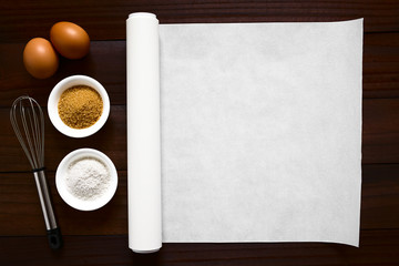 Roll of white baking paper with whisk and baking ingredients such as flour, sugar and eggs on the...