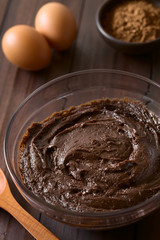 Basic homemade brownie, chocolate cake or cookie dough in glass bowl with cocoa powder and eggs in...