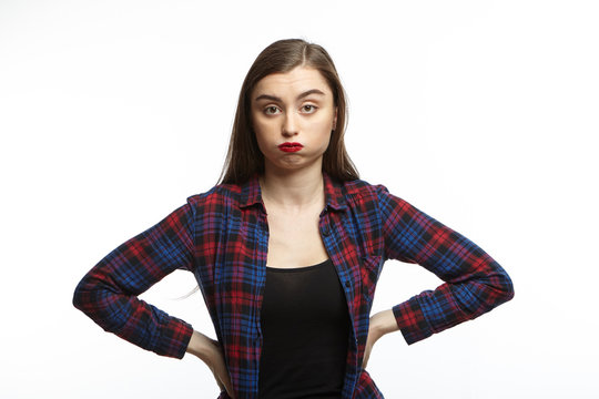 Picture of annoyed young woman wearing plaid shirt over black t-shirt holding hands on her waist and puffing her cheeks, feeling fed up and puzzled with something irritatting. Mimic and grimace