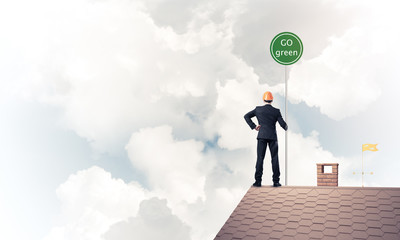 Businessman in suit on house top with ecology concept signboard.