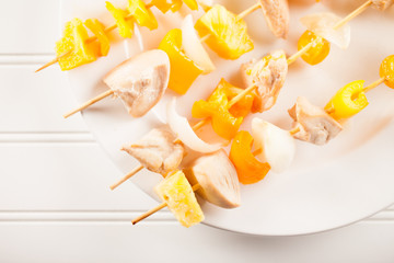 Chicken shish kebab with pineapple and orange bell pepper slices on a white plate white background
