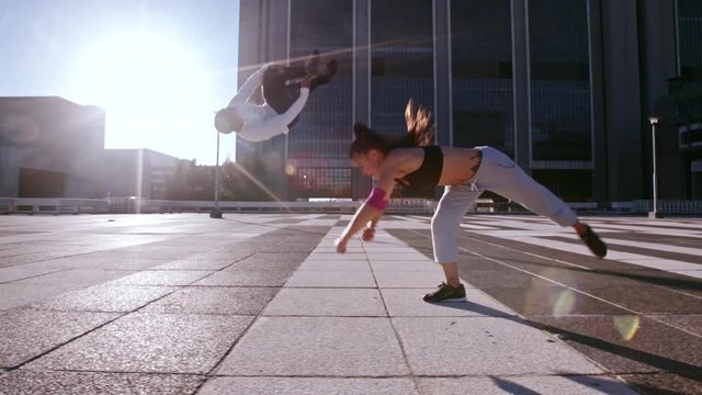 Man and woman doing flips outdoors in city. Urban runners in action practicing parkour in city space.