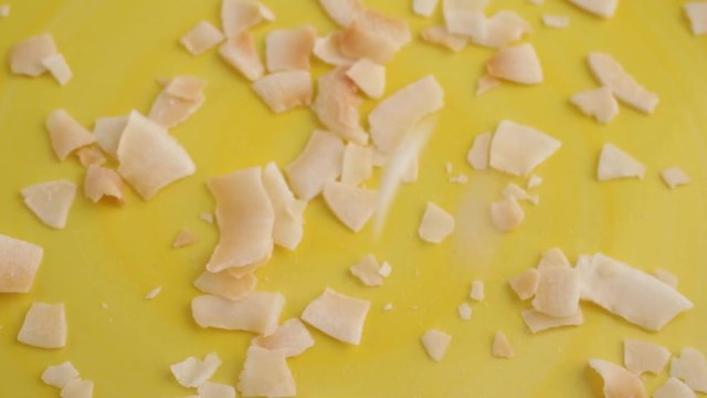 Slow motion video of pouring freshly toasted coconut flakes into a bright yellow dish.