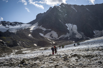 Naklejka premium A group of hiking tourists go along the glacier to the mountain pass. The weather facilitates complex movement in the high-mountainous area. Travelling in the Caucasian Mountains in Georgia