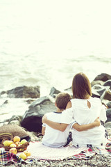 Obraz na płótnie Canvas Mom and son are sitting on a plaid near the sea on a summer day