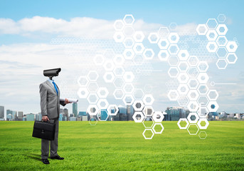 Camera headed man standing on green grass against modern cityscape