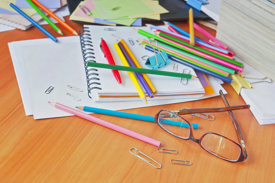 Glasses on the background of colored pencils and paper. The clutter on the desktop.