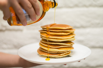 Thick maple syrup pouring onto a stack of fresh pancakes