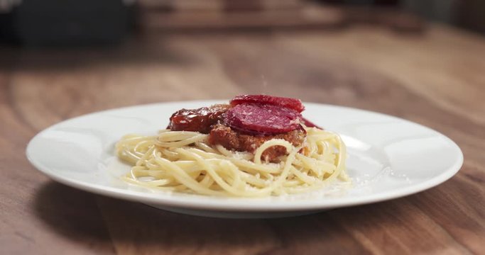 Slow motion closeup shot of fuet falling on spaghetti bolognese