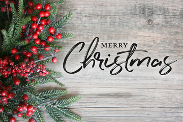Merry Christmas Text with Christmas Evergreen Branches and Berries in Corner Over Rustic Wooden...