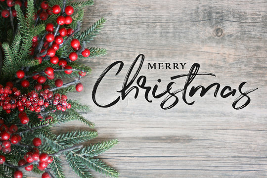 Merry Christmas Text with Christmas Evergreen Branches and Berries in Corner Over Rustic Wooden Background