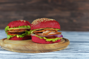 tasty burgers, sandwiches with a red bread, with bacon cheese and salad on a wooden board