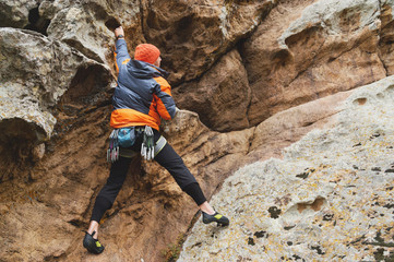 Hipster - climber at the age of climbing up a beautiful rock without insurance and helmet