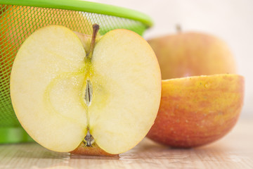 Fresh, juicy apples in the basket and one sliced in half on a wooden base