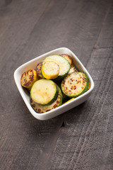 
Small white bowl of roasted squash and zucchini on dark background isolated
