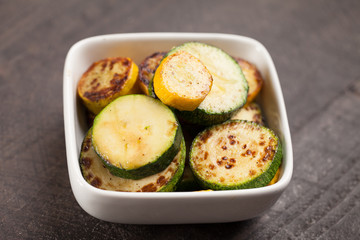 
Small white bowl of roasted squash and zucchini on dark background up close shot
