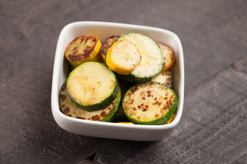 
Small white bowl of roasted squash and zucchini on dark background slightly above shot
