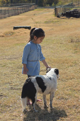 little girl wearing denim outfits let a dog smell a rock  in a farm