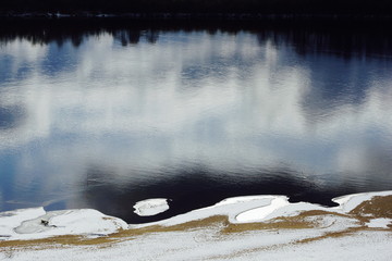 the dark water in the river with the top of the snow bank