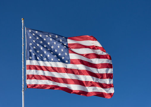 The stars and stripes of the American flag against a dark blue sky. The flag is unfurled by the wind.