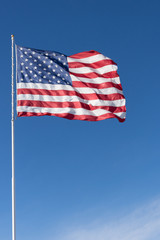 The stars and stripes of the American flag against a deep blue sky. Wind is unfurling the flag.