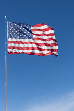 The stars and stripes of the American flag against a deep blue sky. Wind is unfurling the flag.